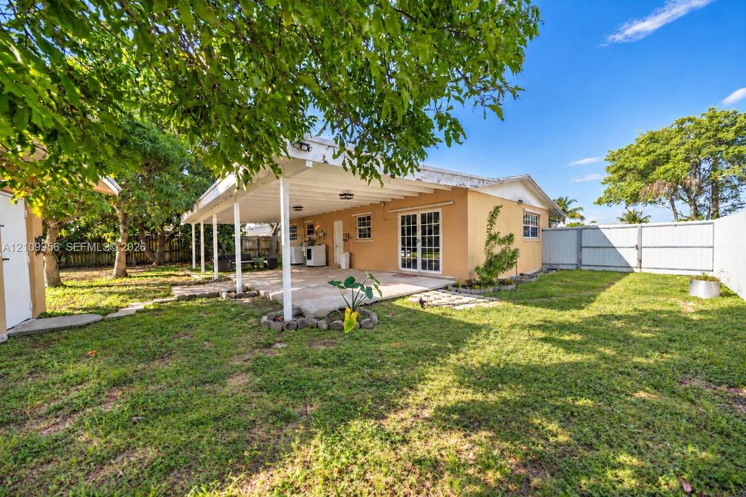 Backyard featuring a covered patio, concrete hardscaping, mature trees, and perimeter fencing