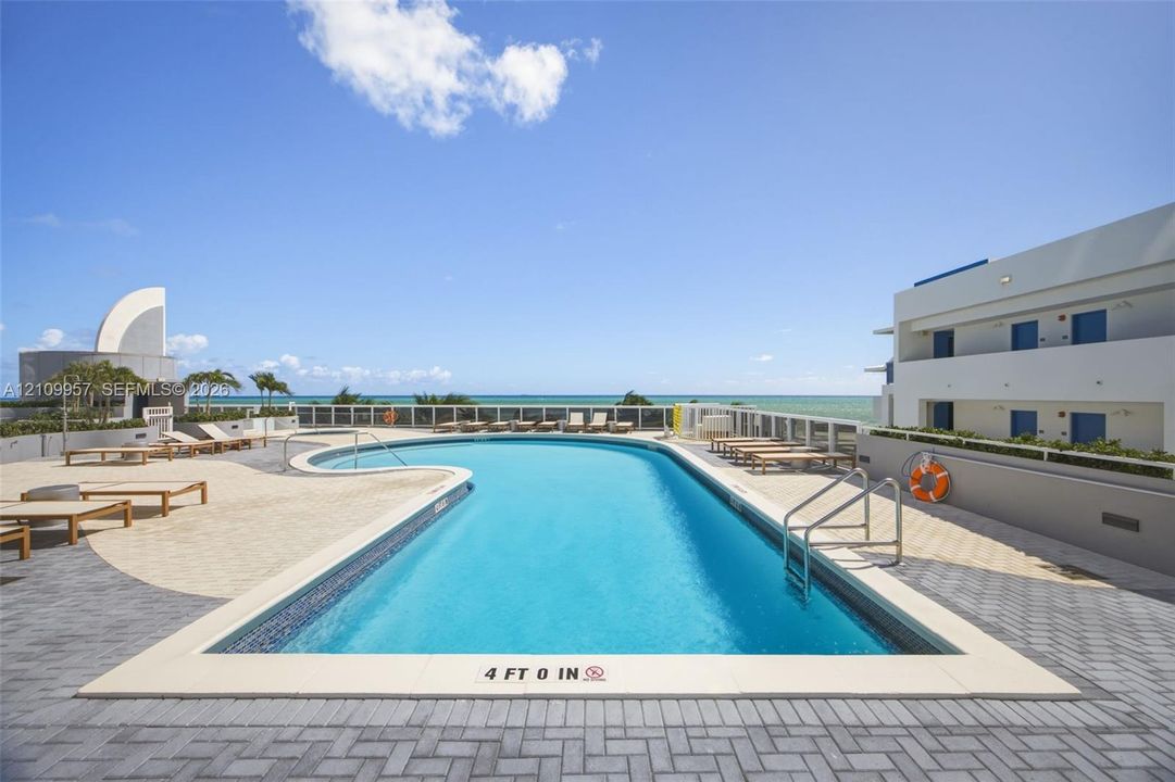 7th floor swimming pool with a stone tile deck, metal perimeter fencing, and an unobstructed ocean backdrop