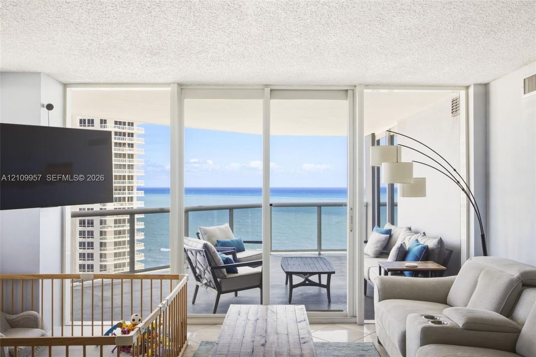 Floor-to-ceiling sliding glass doors opening to a covered balcony with expansive ocean scenery