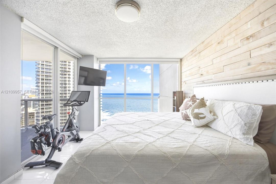 Gorgeous primary bedroom with wood-plank accent wall, polished tile flooring, and expansive ocean horizon