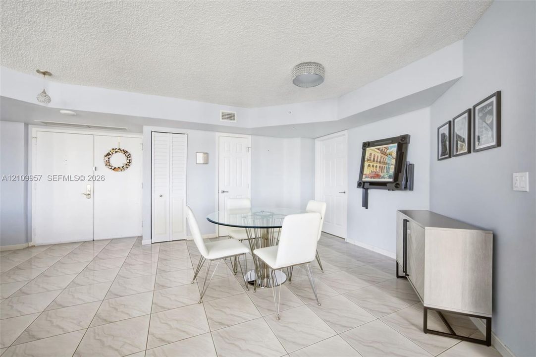 Light-filled interior featuring large-format diagonal tile flooring, multi-panel doors, ceiling-mounted light fixtures, and a textured ceiling finish
