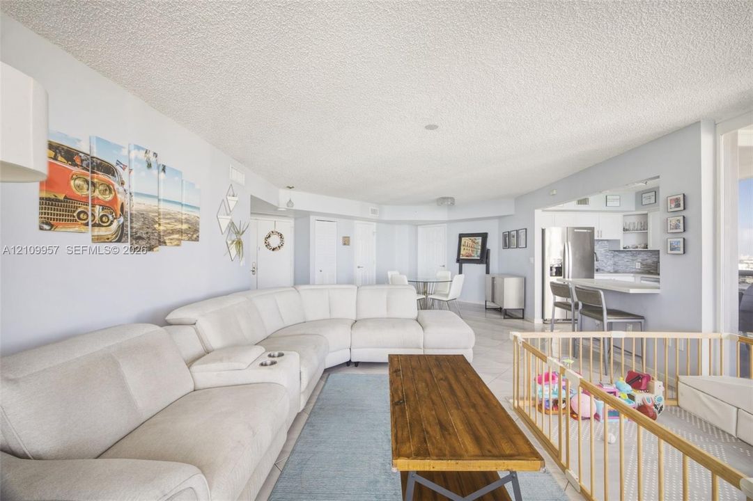 Open-concept interior featuring light-toned tile flooring, recessed lighting, and a kitchen breakfast bar with stone-finish countertops and integrated stainless steel appliances