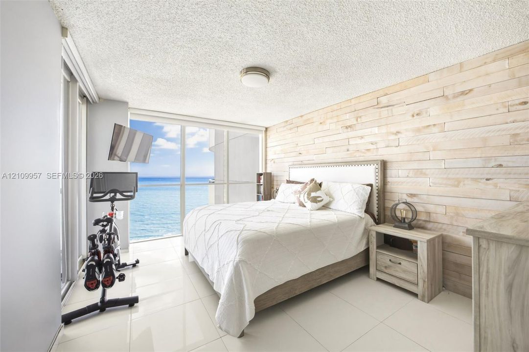 Floor-to-ceiling glass sliding doors, horizontal wood-plank accent wall, polished tile flooring, and coastal ocean horizon