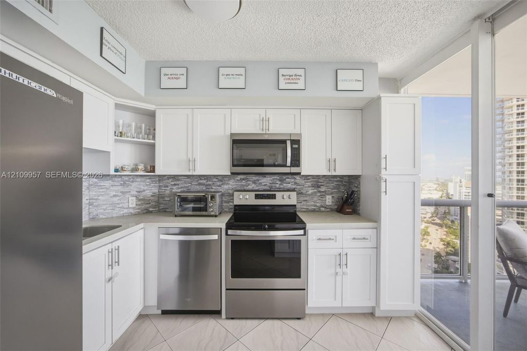 Updated kitchen featuring white shaker cabinetry, stainless steel appliances, neutral countertop surfaces, stone-tiled backsplash, and tile flooring