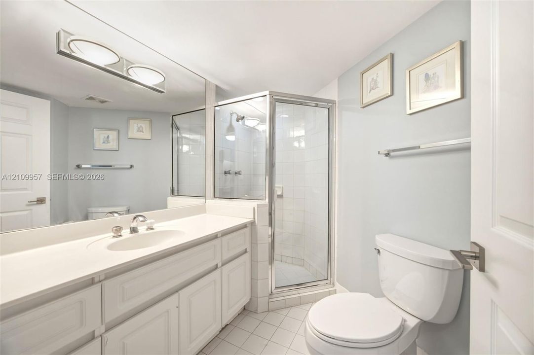Secondary bathroom featuring a vanity with an integrated sink and countertop, a full-width wall mirror, a glass-enclosed shower, and tile flooring
