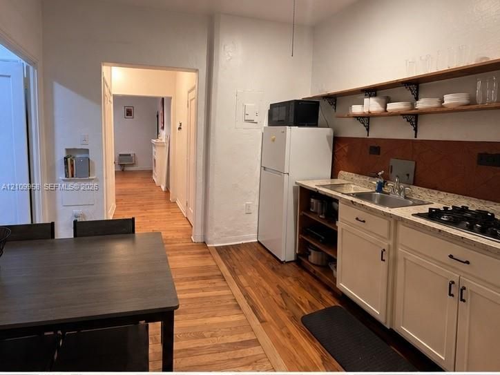 Kitchen featuring wood-finish flooring, stone-finish countertops, white cabinetry, integrated gas cooktop, and open wooden shelving