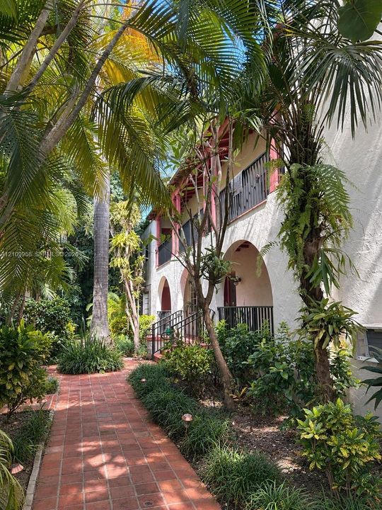 Stucco exterior featuring arched entryways, a terracotta brick walkway, multi-level metal railings, and mature tropical landscaping