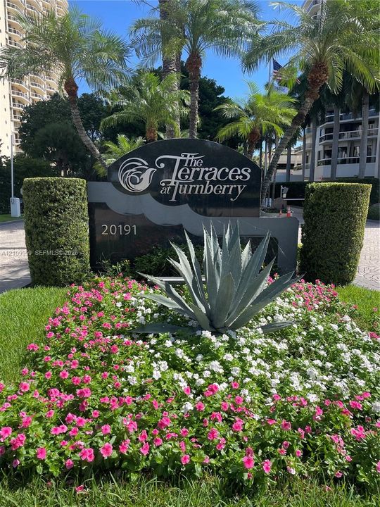 Monument sign for The Terraces at Turnberry featuring polished stone lettering, mature palm trees, sculpted hedges, and landscaped flower beds