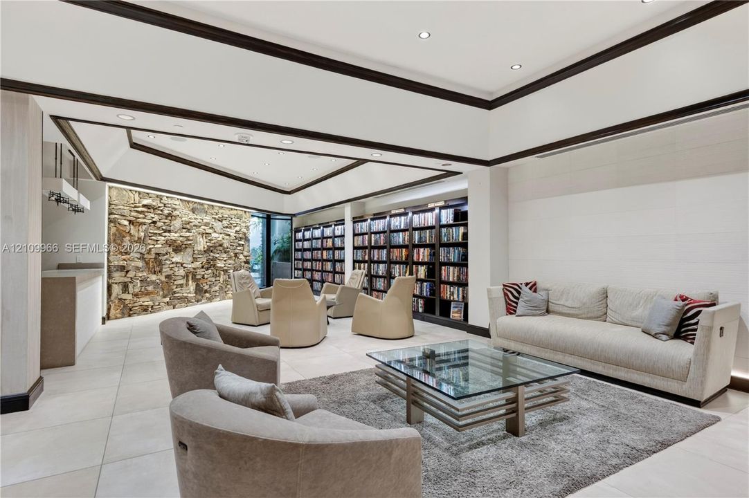 Spacious room featuring a tiered tray ceiling, large-scale stone accent wall, extensive built-in floor-to-ceiling shelving, recessed lighting, and large-format tile flooring