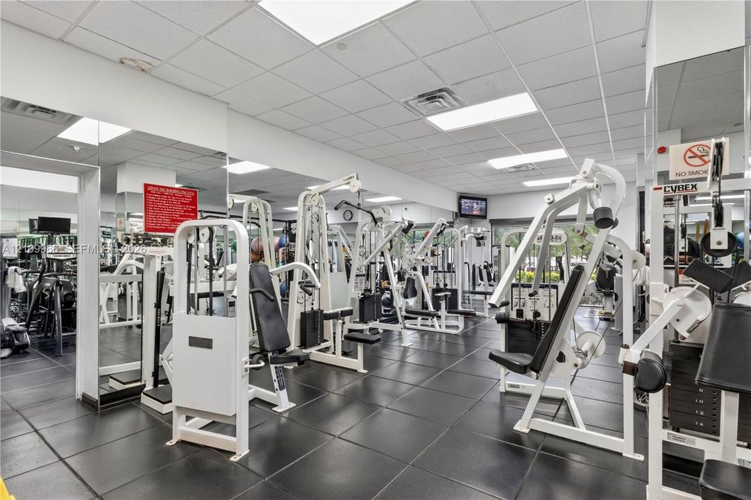 Fitness center featuring rubberized floor tiling, wall-to-wall mirrors, recessed lighting, and a drop ceiling
