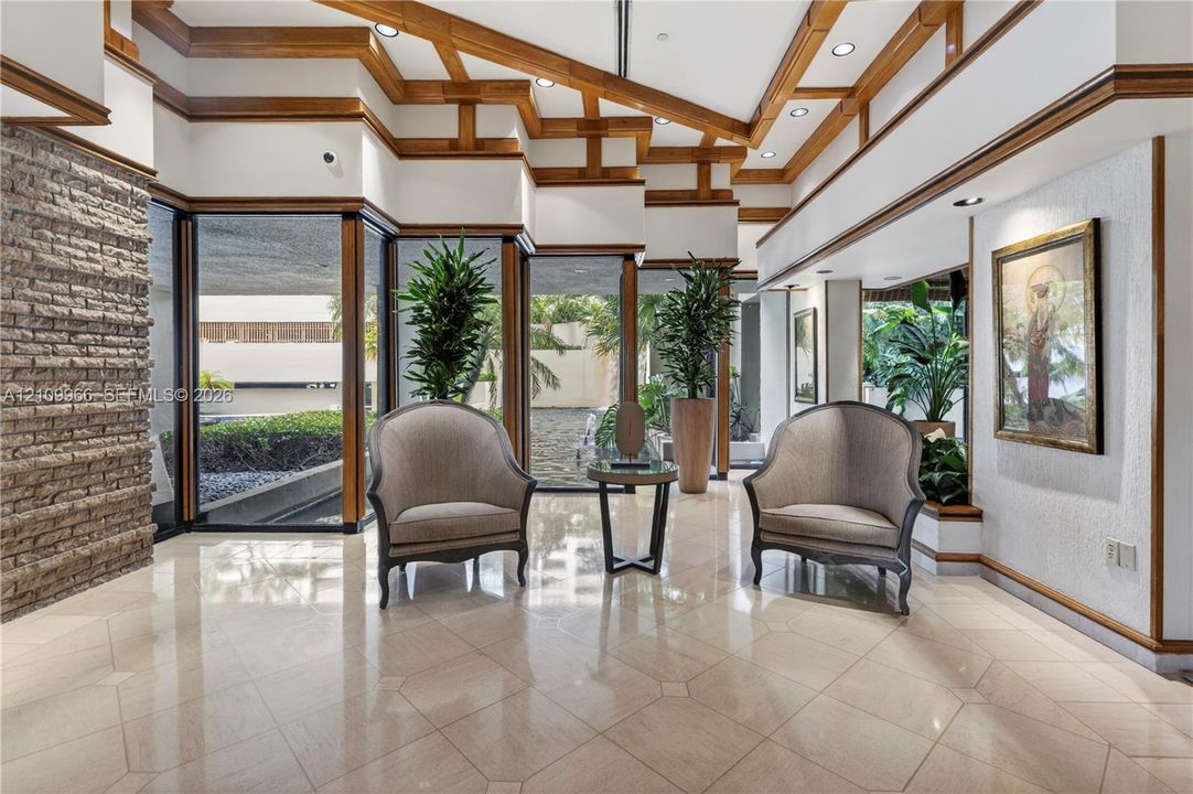 Vaulted ceiling with exposed wood-beam detailing, polished stone tile flooring, expansive floor-to-ceiling windows, and integrated stone masonry accent wall
