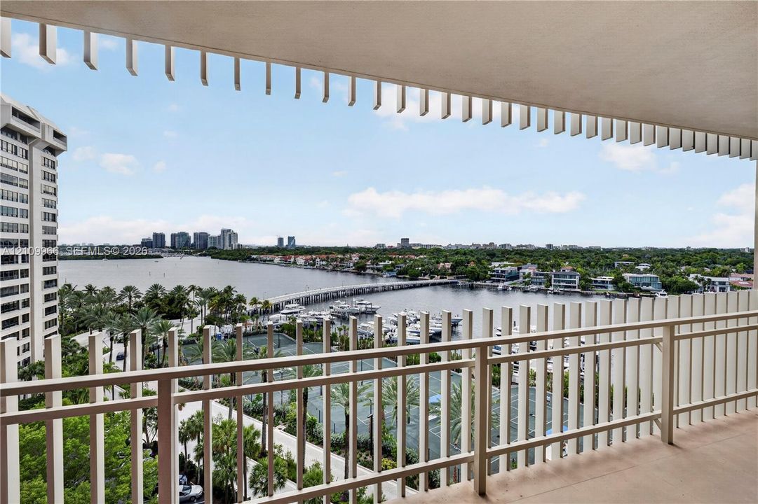 Covered balcony featuring vertical privacy screening and metal railing, overlooking a marina and waterfront landscape