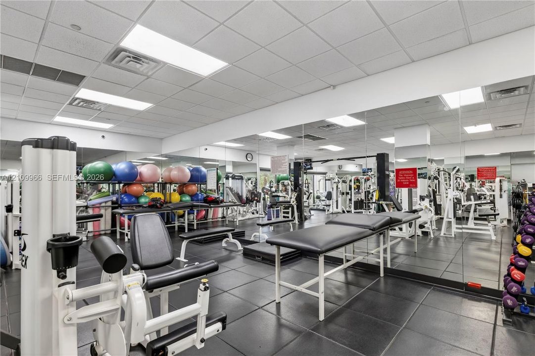 Fitness facility featuring wall-to-wall mirrors, durable rubberized tile flooring, and drop ceiling with recessed lighting