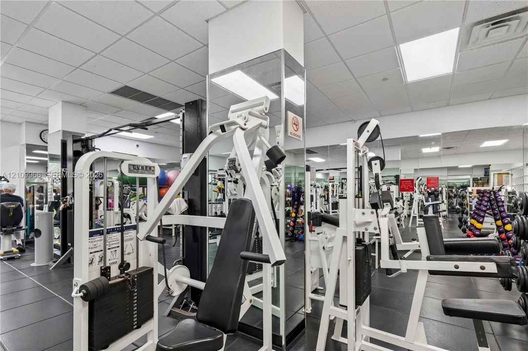 Fitness center featuring grid ceiling tiles, wall-to-wall mirrors, and durable rubber flooring