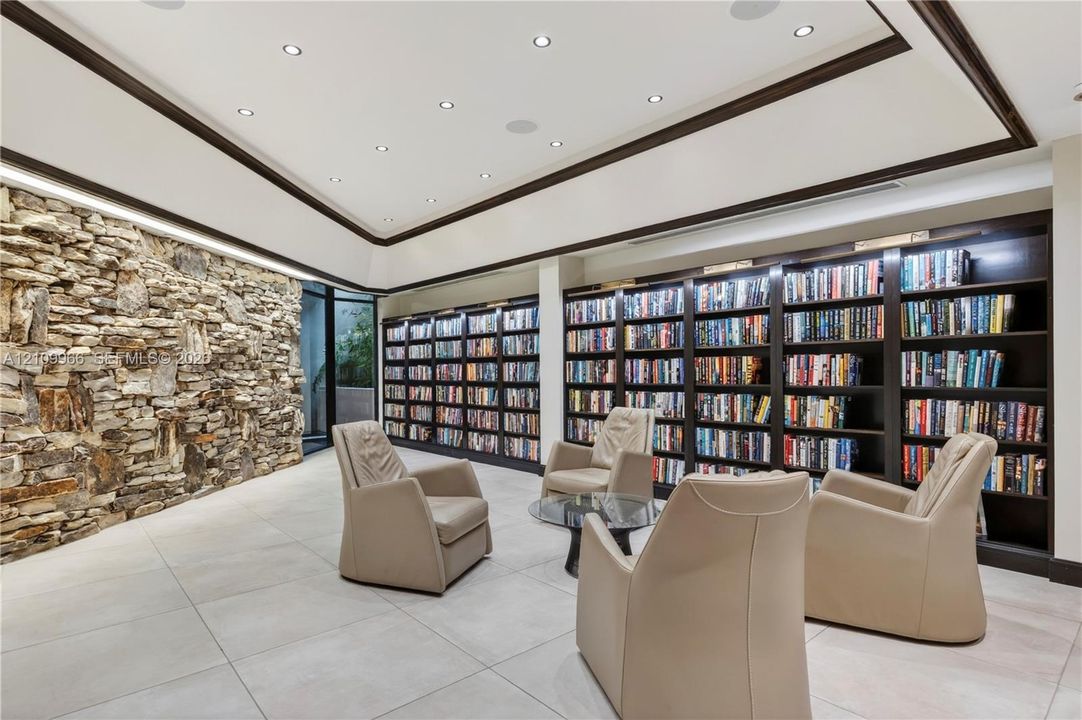 Floor-to-ceiling dry-stack stone accent wall, expansive built-in dark wood shelving, recessed lighting, and large-format tile flooring