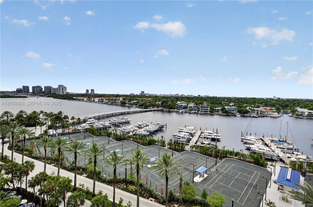 Waterfront property featuring a private marina with multiple boat slips and professional tennis courts surrounded by mature palm trees