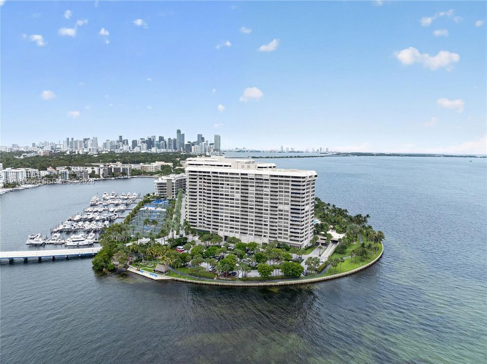Waterfront high-rise building situated on a peninsula, featuring a private marina with boat slips, multiple hard-court tennis facilities, lush mature landscaping, and covered parking