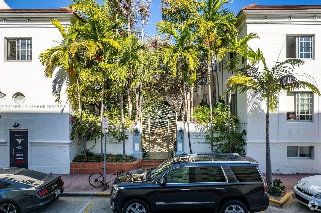Stucco facade with articulated molding, decorative metal gate, and mature palm trees
