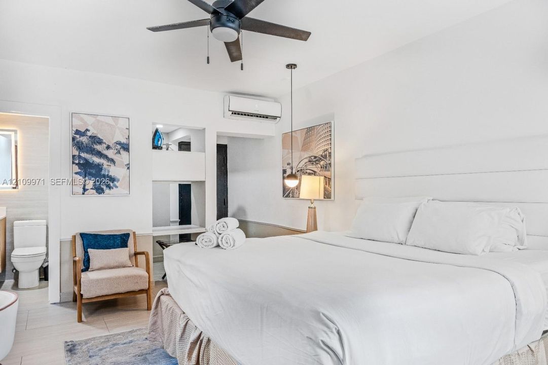 Neutral-toned interior featuring a recessed wall niche with built-in shelving, a modern ceiling fan, a wall-mounted ductless air conditioning unit, and a pendant light fixture