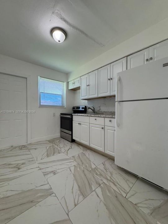 Kitchen featuring white cabinetry, stone-finish countertops, stainless steel appliances, and large-format tile flooring