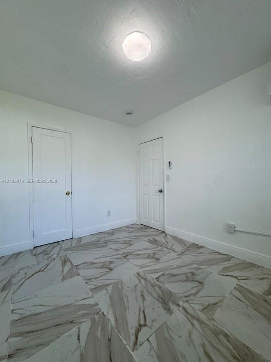 Large-format, high-contrast tile flooring, white interior doors, and a circular flush-mount ceiling light fixture