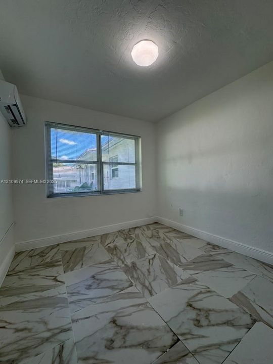 Room featuring large-format patterned stone-finish tile flooring, wall-mounted ductless climate control unit, and flush-mount ceiling lighting