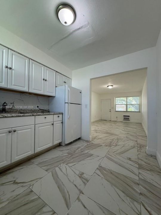 Kitchen featuring white cabinetry, speckled stone countertops, and large-format porcelain tile flooring with veined detailing