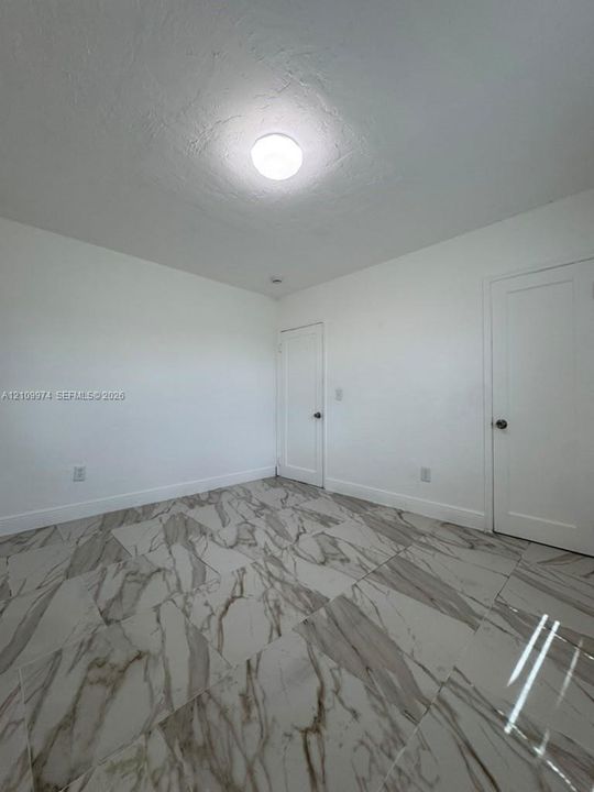Neutral interior featuring large-format stone-pattern tile flooring, crisp white walls, and two solid-core interior doors with hardware