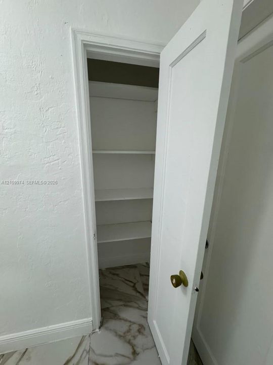 Storage closet featuring white interior shelving, a paneled door, and polished stone-finish flooring