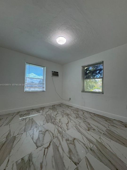 Large-format tile flooring featuring high-contrast veining, two dual-pane windows, and a central flush-mount ceiling light