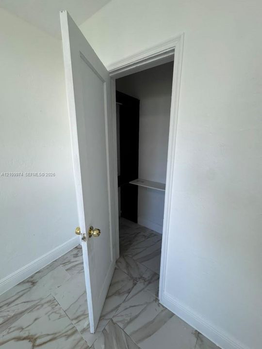 Storage area featuring large-format tile flooring with veining, a painted panel door with brass-finish hardware, and built-in shelving