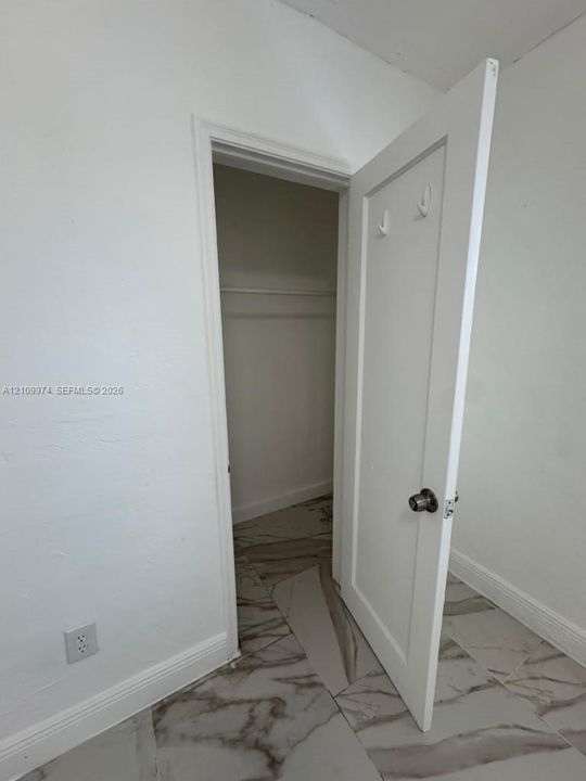 Storage area featuring large-format tile flooring with a marble-style finish, a built-in clothing rod, and a solid-core panel door with metallic hardware