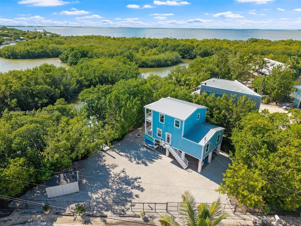 Elevated residence featuring a metal roof, exterior stairway, stone-surface driveway, and onsite storage structure, situated within proximity to coastal waterways and mangroves