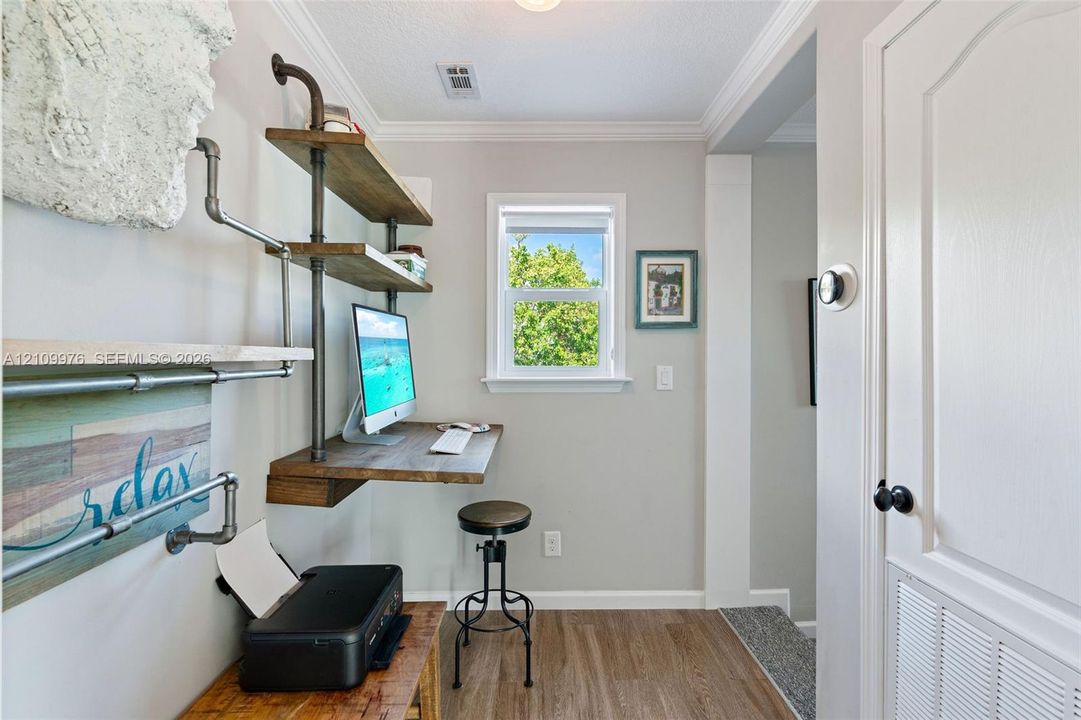 Built-in industrial-style shelving with wood-finish surfaces, wall-mounted desk, crown molding, and wood-finish flooring