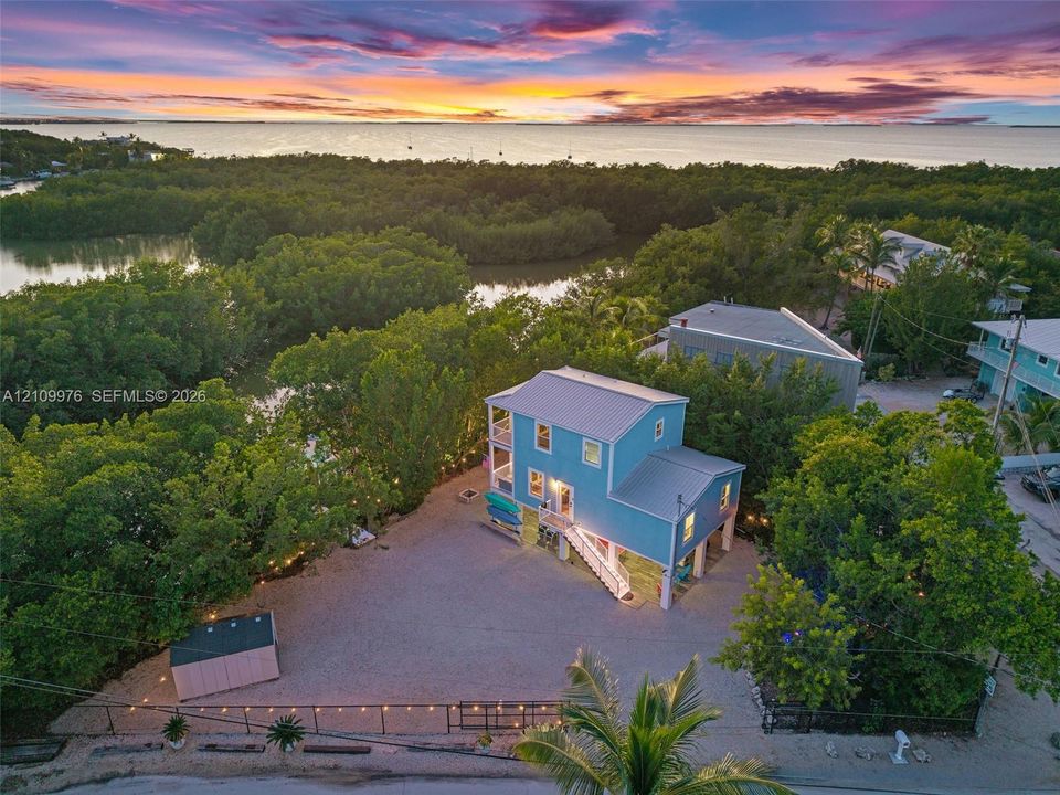 Two-story residence featuring a metal roof, elevated structural foundation, gravel grounds, and perimeter fencing