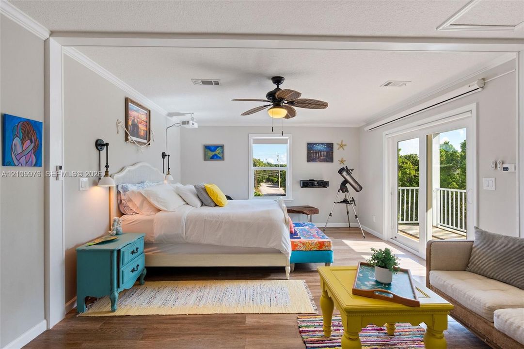 Living space featuring wood-finish flooring, a ceiling fan with integrated lighting, wall-mounted light fixtures, and glass sliding doors providing access to an exterior balcony