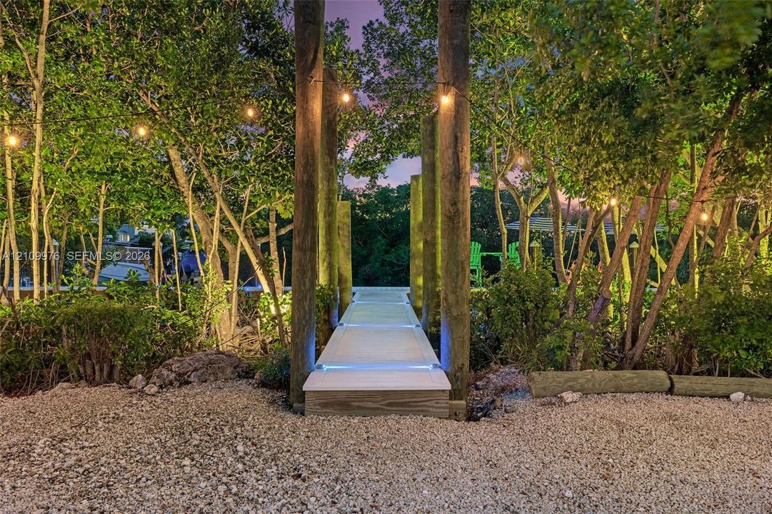 Gravel surface ground cover, wooden support pilings, elevated composite walkway, and integrated path lighting