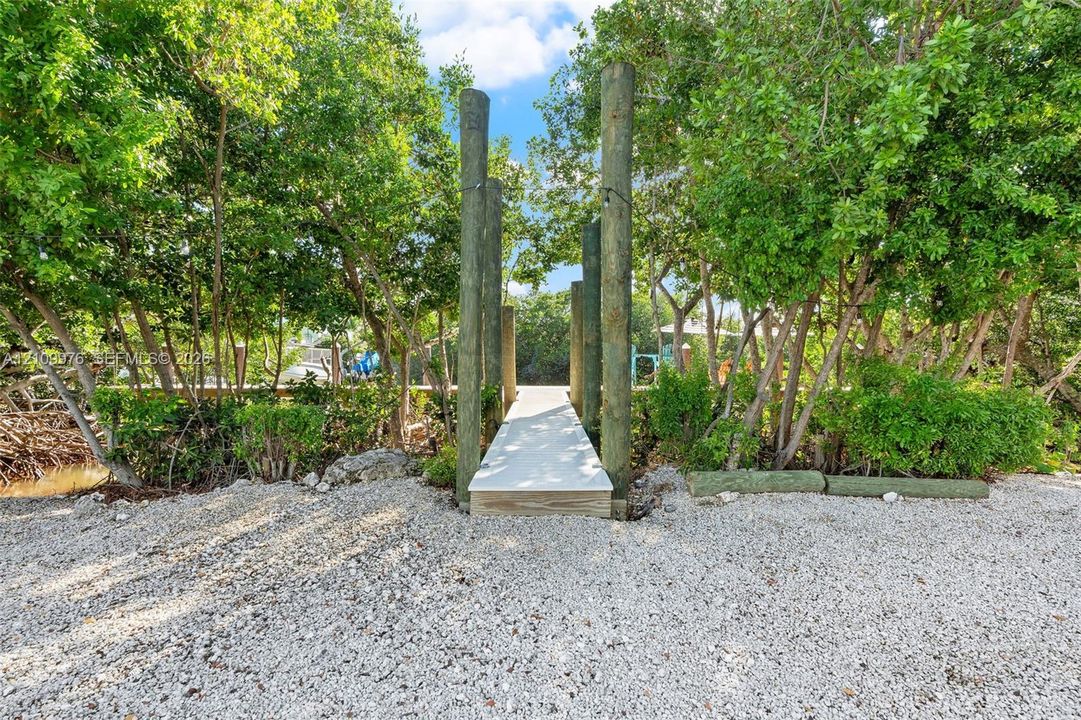 Waterfront dock featuring pilings, light-colored decking, and natural shell shoreline bordered by mature trees and native vegetation