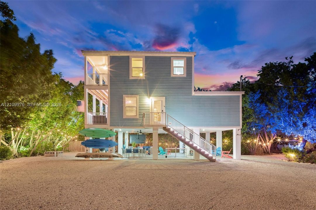 Multi-level exterior featuring light blue siding, dual stacked covered balconies, and an elevated ground-level concrete patio with metal railings