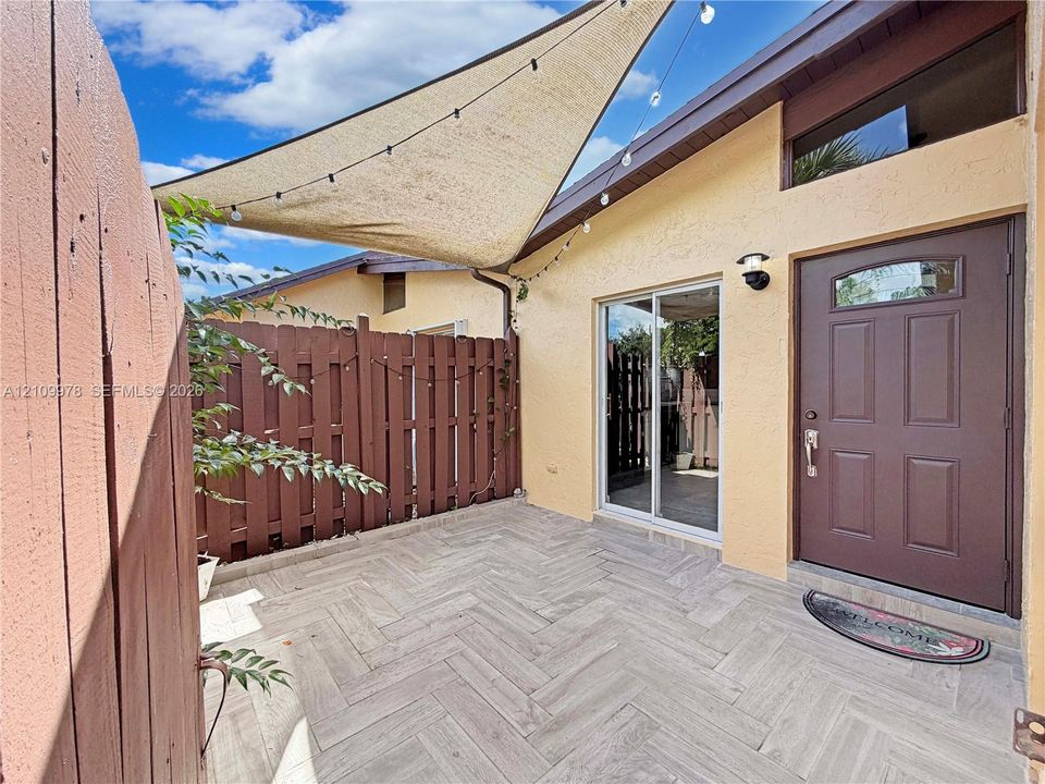 Private courtyard featuring herringbone-patterned tile flooring, a solid wood privacy fence, sliding glass door, and a six-panel exterior door with a transom window