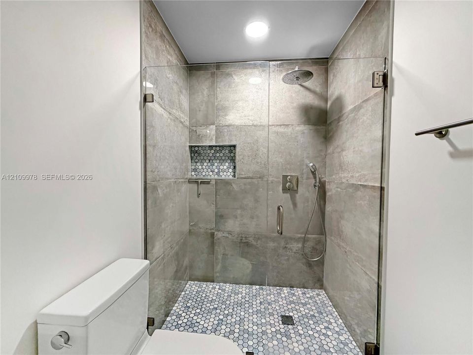 Walk-in shower featuring large-format wall tile, a mosaic-tiled floor and inset niche, a frameless glass enclosure, and dual-function rainfall and handheld shower fixtures