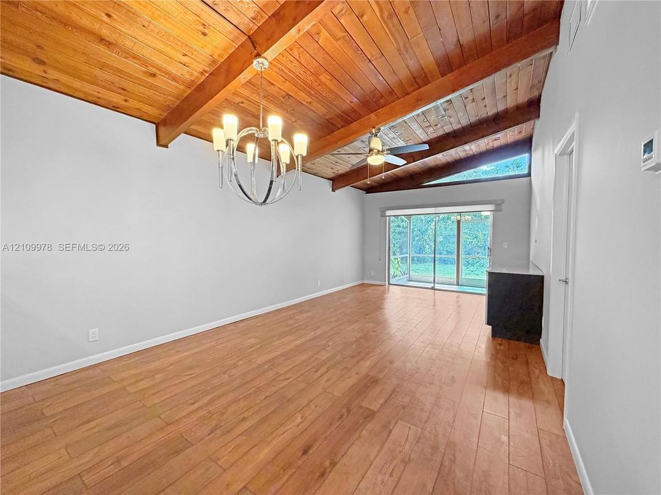 Vaulted ceiling with exposed wood beams, wood-finish flooring, metal chandelier, ceiling fan, and sliding glass doors