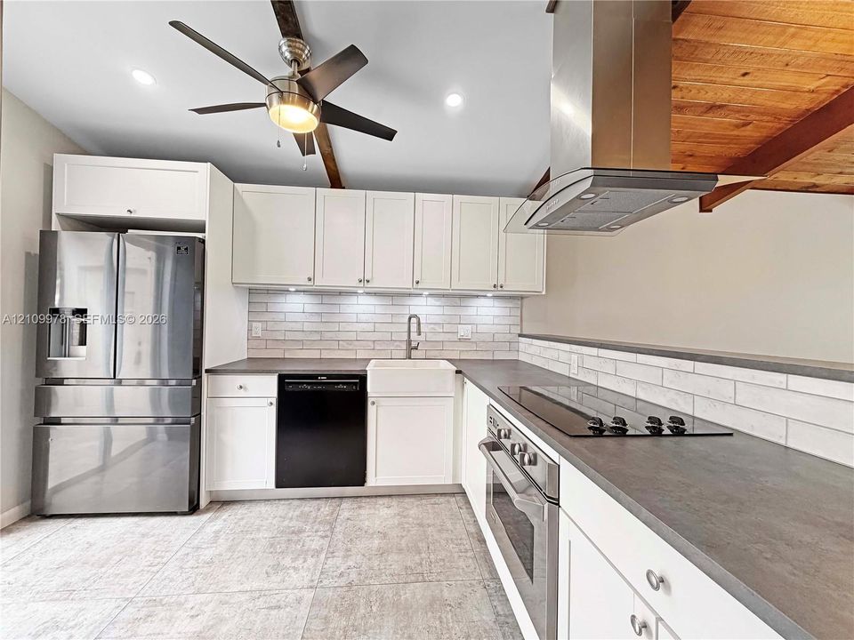Kitchen featuring shaker-style cabinetry, stainless steel appliances, apron-front sink, brick-style tile backsplash, and wood ceiling beams