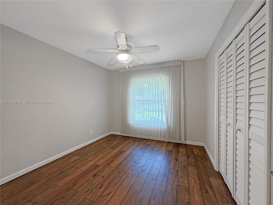 Room featuring wood-finish flooring, white louvered closet doors, and a ceiling fan with integrated lighting