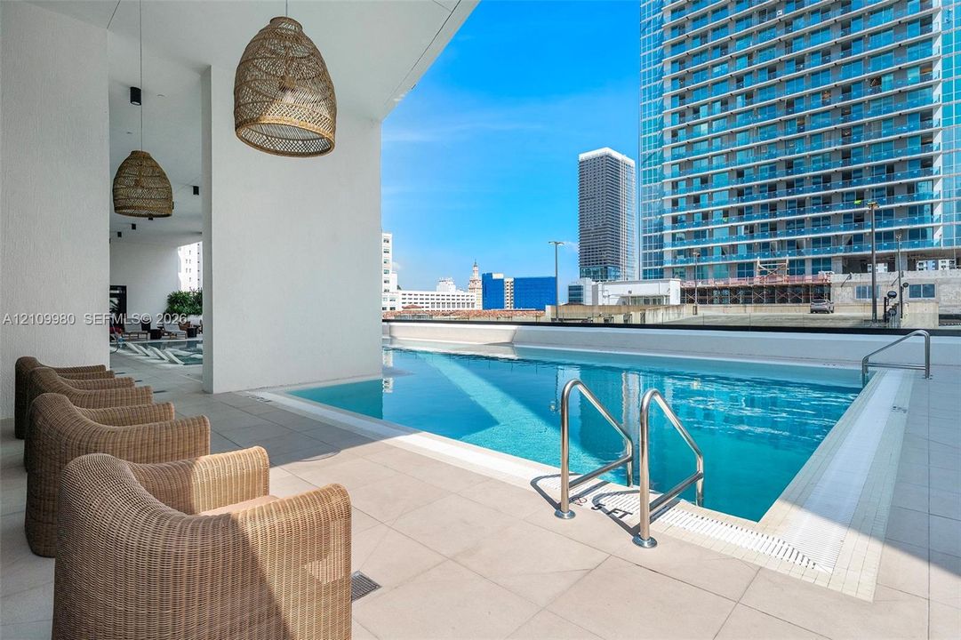 Elevated infinity-edge pool featuring large-format tile decking, stainless steel handrails, and woven pendant lighting fixtures