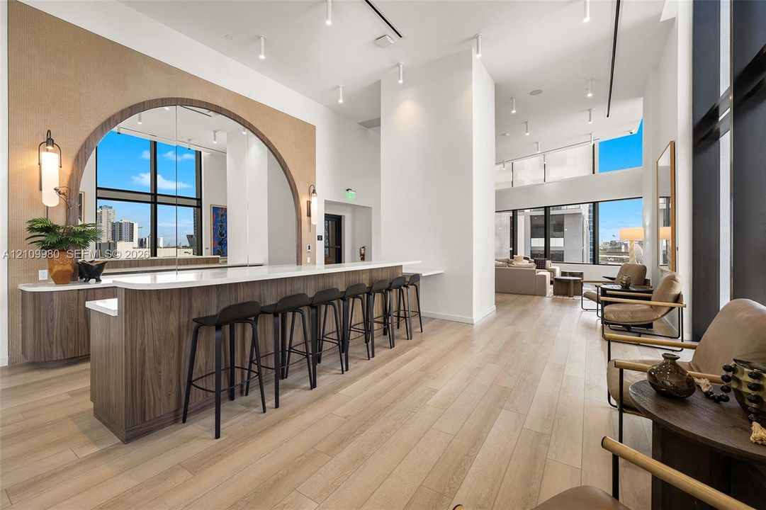 Built-in wet bar featuring wood-finish cabinetry, a white countertop, an arched mirrored backsplash, and wood-finish flooring throughout the expansive area with floor-to-ceiling windows