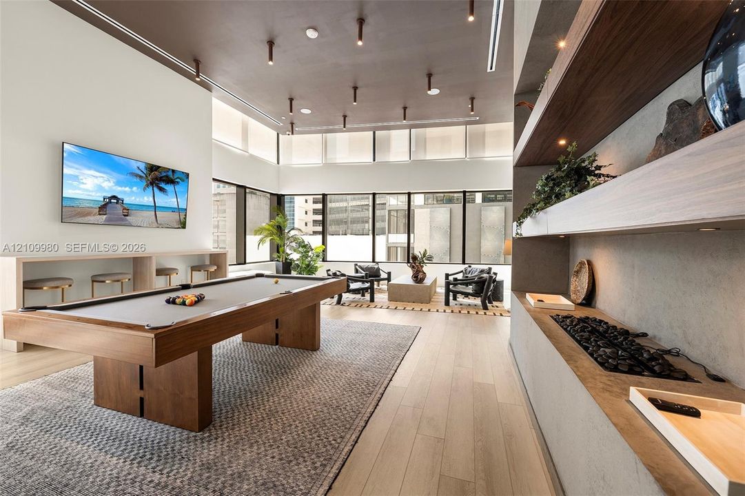 Expansive room featuring floor-to-ceiling windows, wood-finish flooring, a coffered ceiling with recessed lighting, and a built-in stone-surround fireplace with integrated wooden shelving