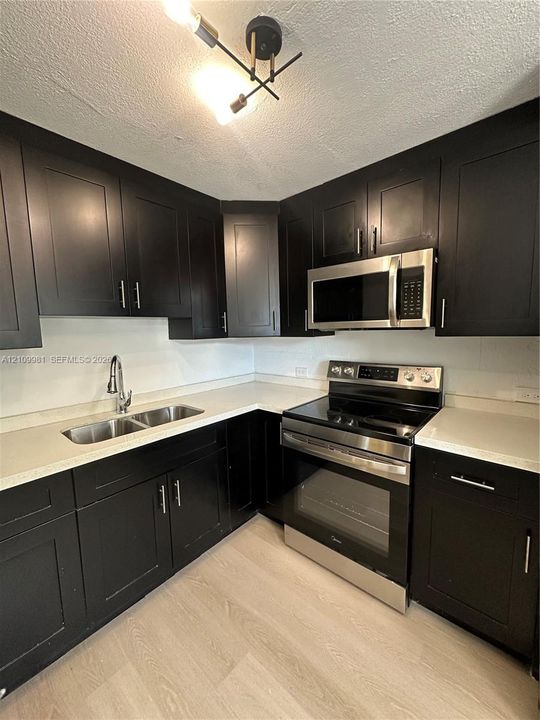 Kitchen featuring matte black shaker cabinetry, light-toned countertops, stainless steel appliances, a dual-basin undermount sink, and contemporary multi-arm light fixture