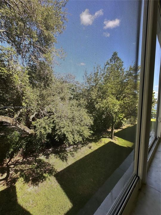 Large floor-to-ceiling sliding glass doors with screen panels, overlooking a landscaped exterior with mature trees and a grass lawn