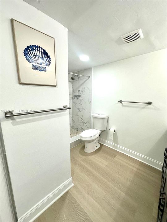Full bathroom featuring wood-finish flooring, a glass-enclosed shower with stone-patterned wall tile, and brushed nickel hardware